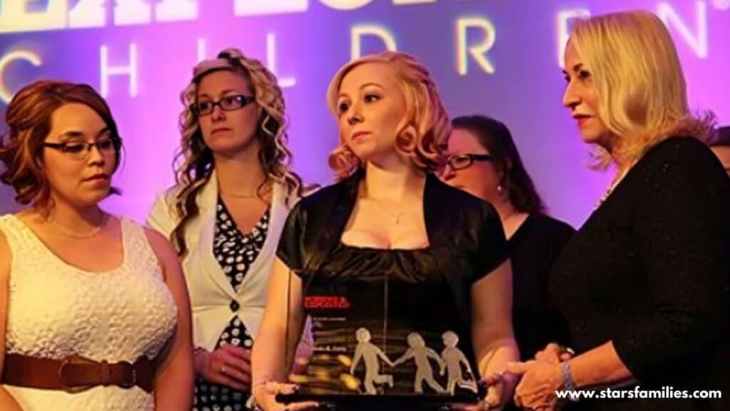 Amanda Berry and Marco Fabián stand together on a stage. Amanda is wearing a blue dress, while Marco is dressed in a suit. The background features large text that reads "MISSING & EXPLOITED CHILDREN." They are holding a plaque or award with a design that includes two child-like figures. The setting appears to be an award ceremony or recognition event.