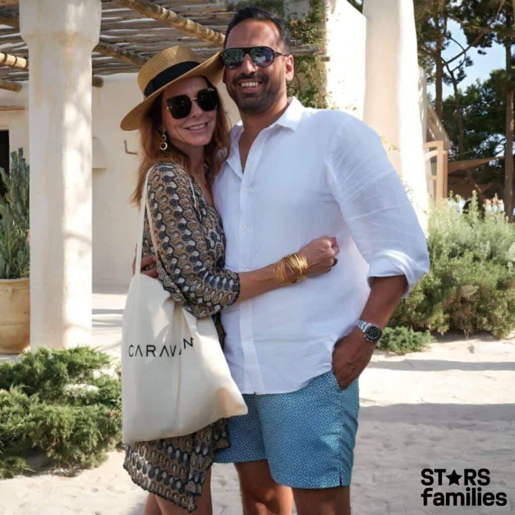 Charlotte Jones, wearing a patterned dress and a straw hat, stands close to her husband, who is dressed in a white button-up shirt and blue patterned shorts. Charlotte carries a beige tote bag with the text "CARAVAN" on it.