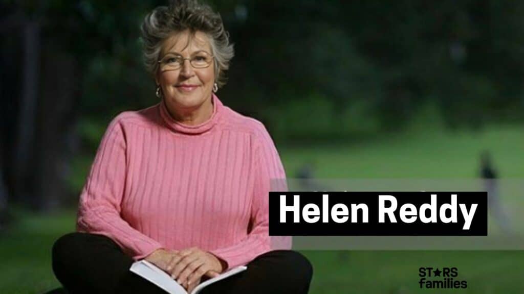 Helen Reddy sits outdoors on a grassy area, wearing a pink sweater and black pants, while holding an open book.