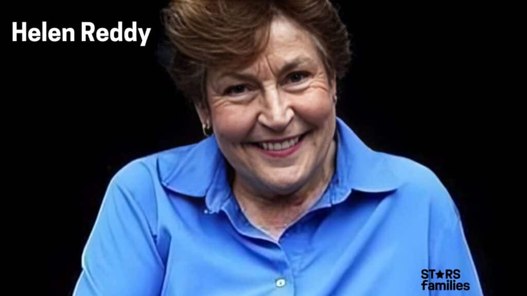  Helen Reddy, wearing a blue button-up shirt with rolled-up sleeves, is seen with a black background.