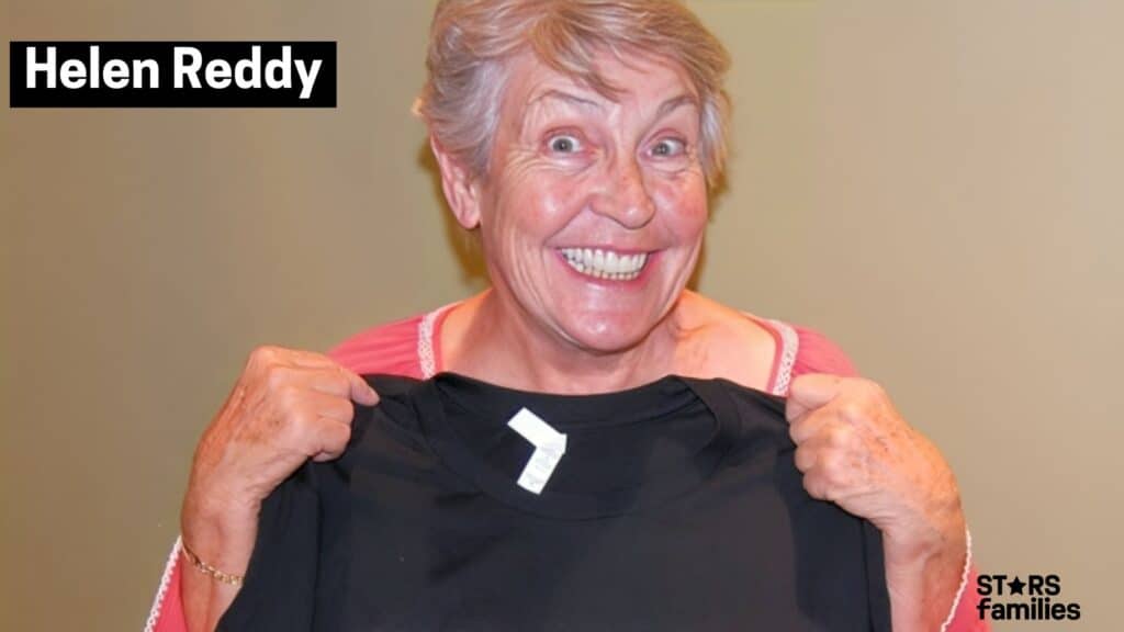 Helen Reddy holds up a black T-shirt while wearing a pink top with white trim.