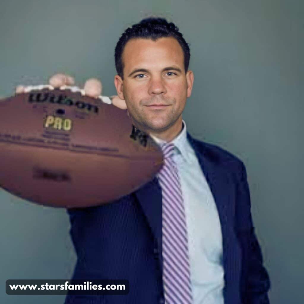 John Cerasani, dressed in a dark suit with a light blue shirt and a purple striped tie, holds a Wilson Pro football, extending it towards the camera.