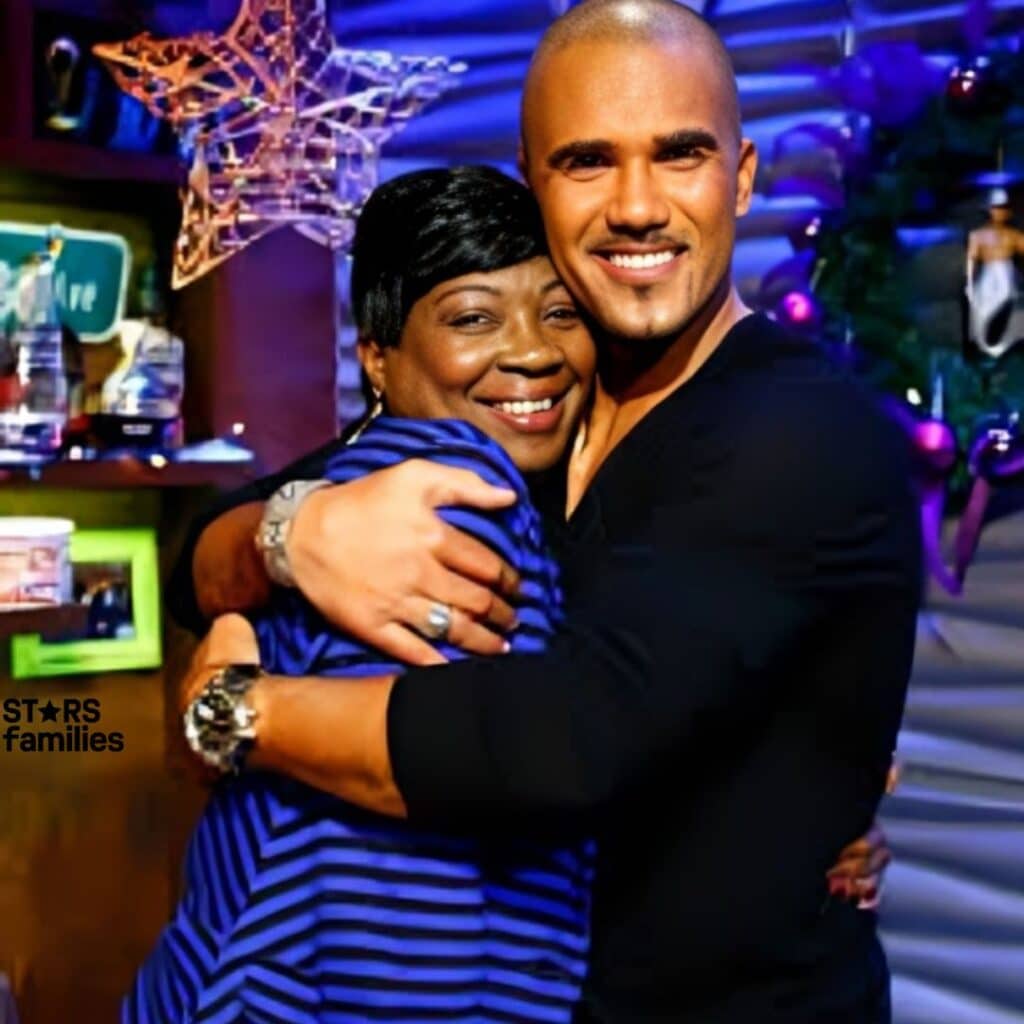 In a festive indoor setting, Sweet Brown, dressed in a black shirt and a watch, hugs Marco Fabián, who is wearing a blue and black striped shirt. The background features a star-shaped decoration, a shelf with various items, and a Christmas tree with ornaments.