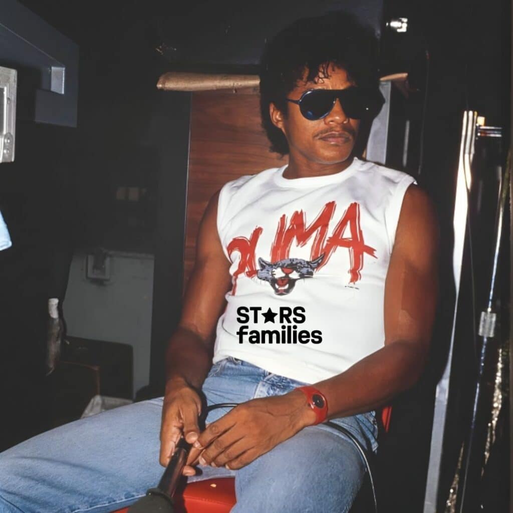 in old picture Parker McCollum, wearing a white sleeveless shirt with "PUMA" written in red, sits on a red chair holding a microphone.