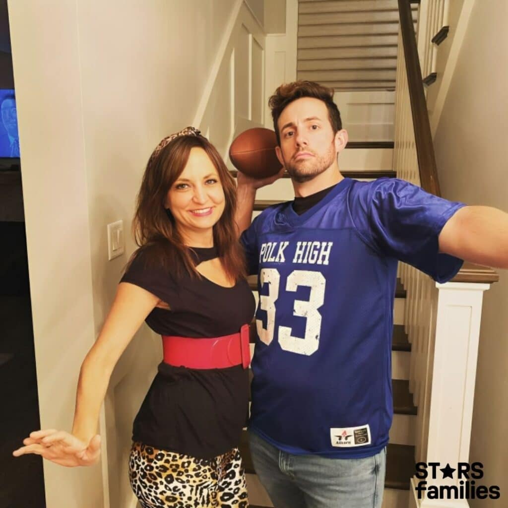 Steve Hamilton, wearing a blue football jersey with the text "POLK HIGH" and the number "33" on it, holds a football and stands next to his wife, who is wearing a black top, a red belt, and leopard print pants. They are posing in front of a staircase.