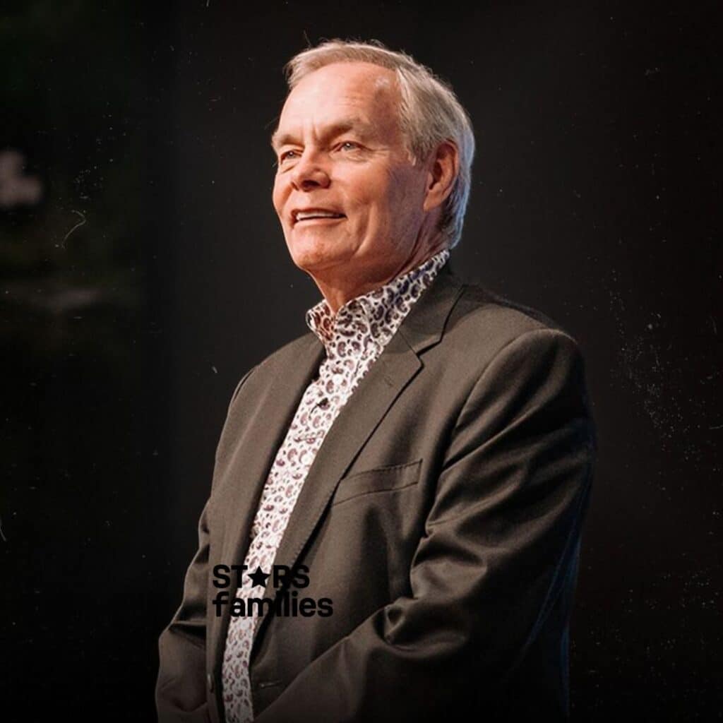 Andrew Wommack, wearing a dark suit jacket over a patterned shirt, is positioned against a dark background.