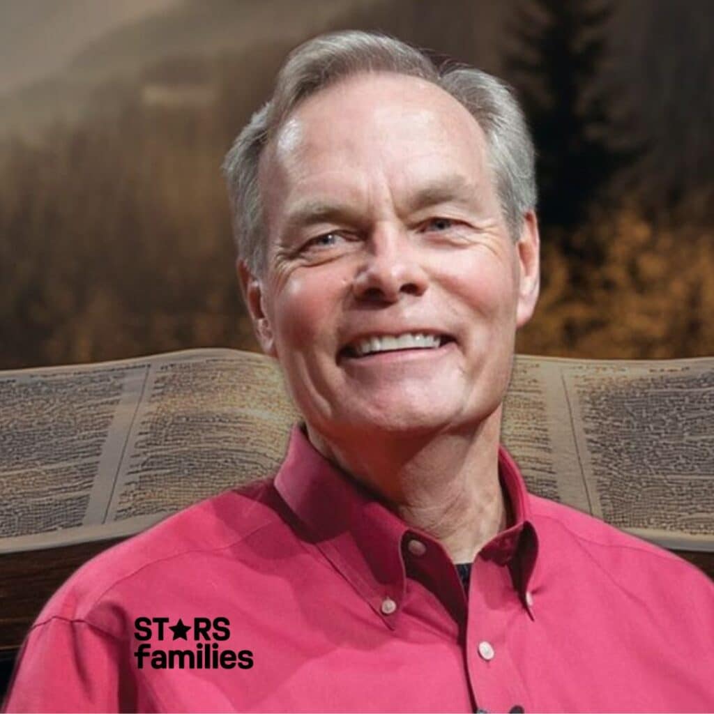 Andrew Wommack, wearing a red shirt . he is seated at a desk with an open book, likely a Bible, in front of him.