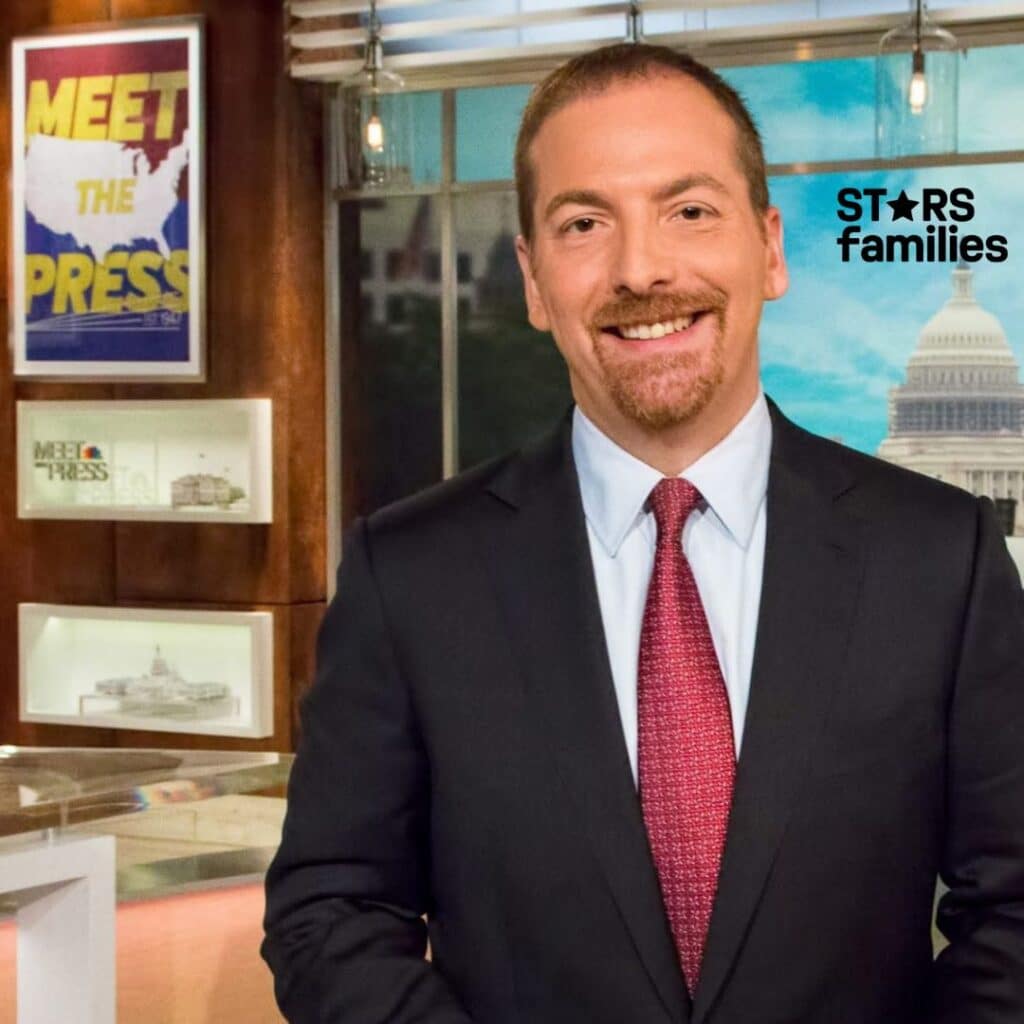 Chuck Todd, wearing a dark suit and red tie, stands in a television studio with a large window view of the U.S. Capitol building. The background includes framed posters, one displaying the text "MEET THE PRESS" with a map of the United States, and another with "MEET THE PRESS" and an image of the White House.