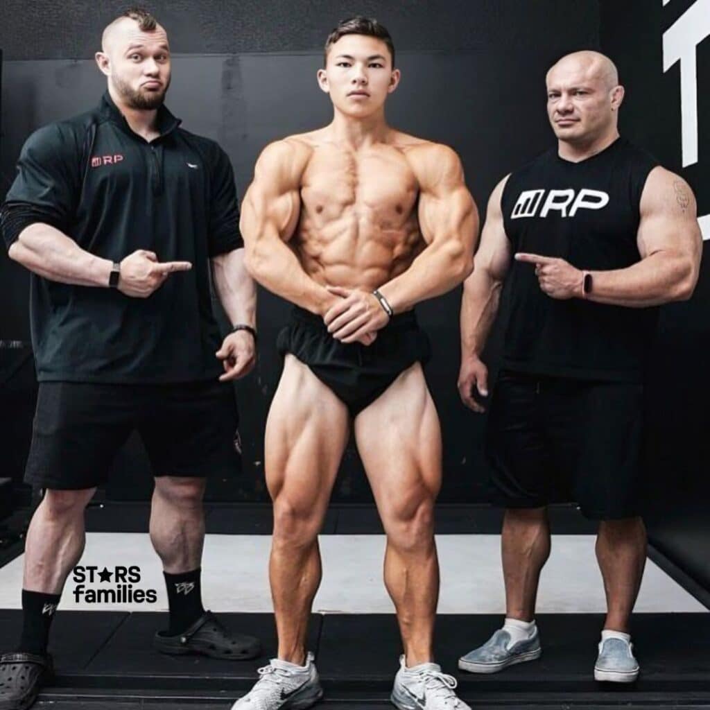 Mike Israetel and his friends are in a gym setting, wearing black fitness attire. 