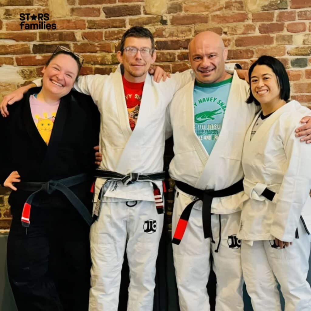  Mike Israetel and his friends are posing in a martial arts dojo. Mike Israetel is wearing a white gi with a black belt, while his wife is dressed in a white gi with a black belt.