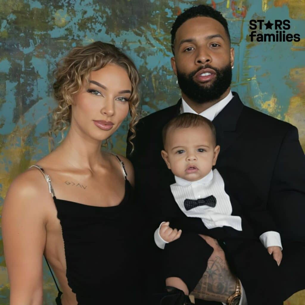 Lolo Wood, her husband, and their son pose for a family portrait. Lolo is wearing a stylish black dress, her husband is dressed in a black suit, and their son is in a cute black suit with a bow tie.