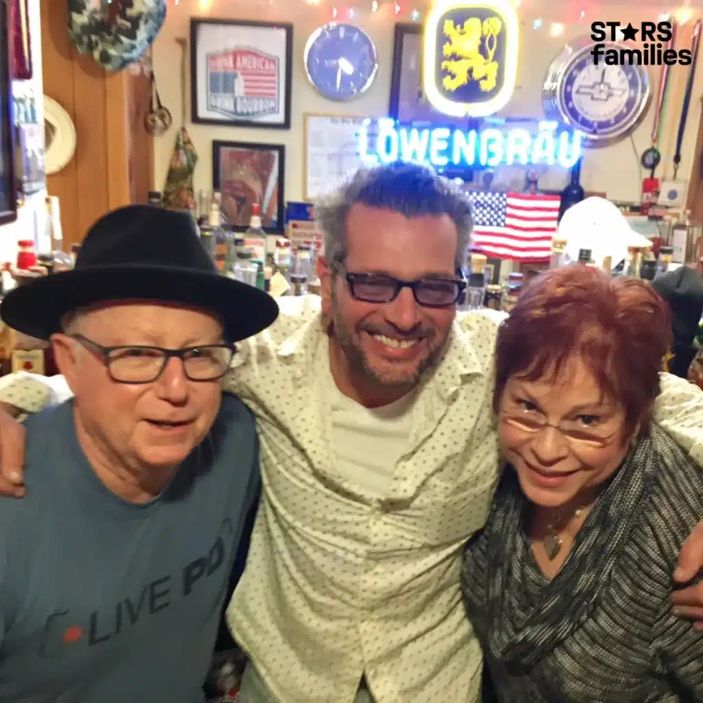 A photo captures Scott Lobaido alongside two others, all three smiling and posing together in a cheerful setting.
