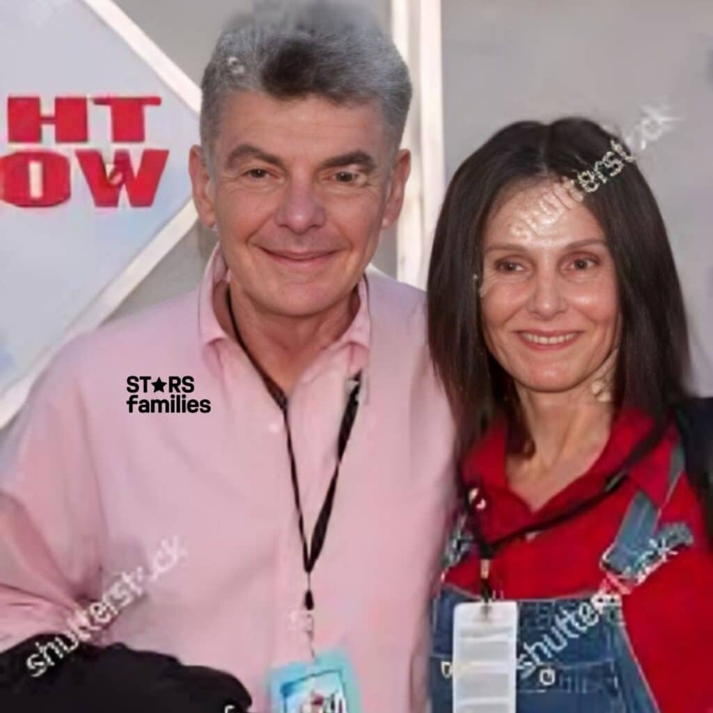 Paula Prentiss and Richard Benjamin stand together in a cozy indoor setting. Paula is wearing a black outfit, and Richard is dressed in a casual shirt and pants.