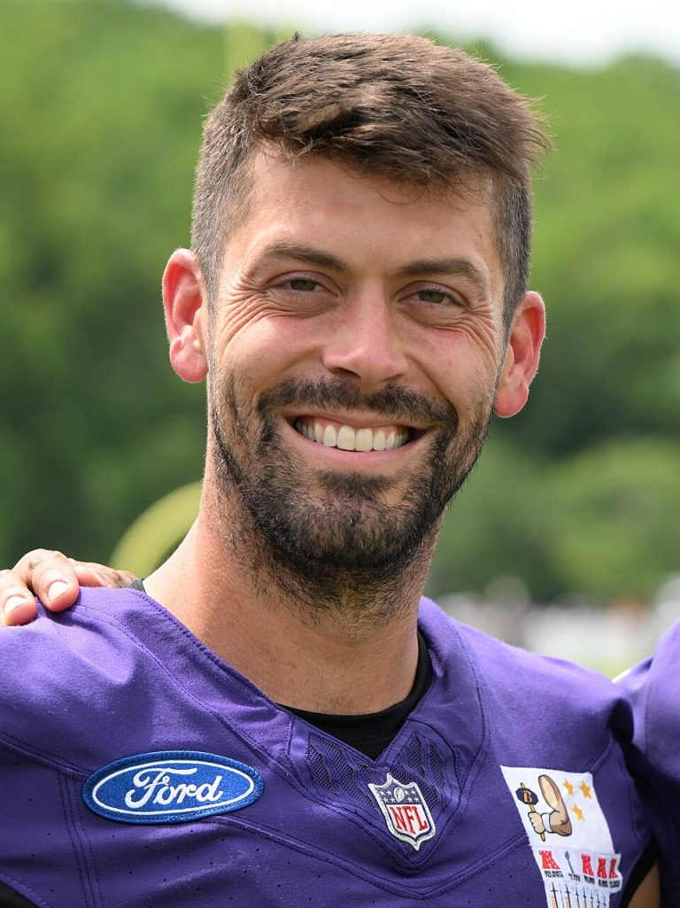 Kicker Justin Tucker smiling in a purple Baltimore Ravens practice jersey at training camp in July 2024